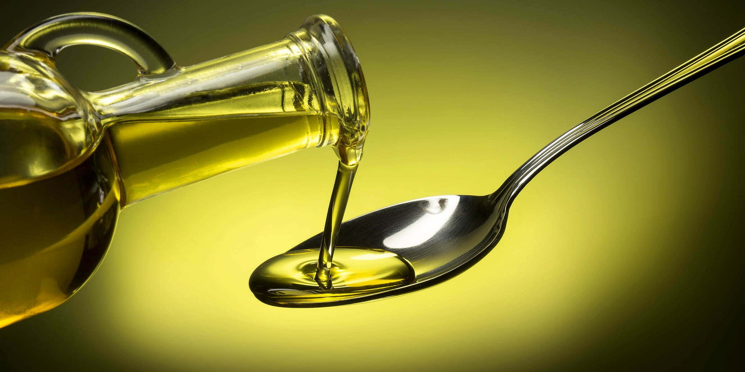 bottle pouring oil in a spoon on green background